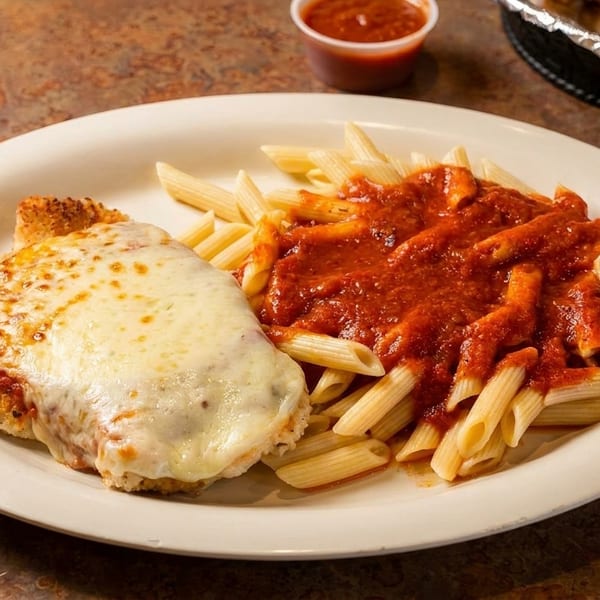 Chicken parmesan with melted cheese and a side of penne pasta with red sauce.