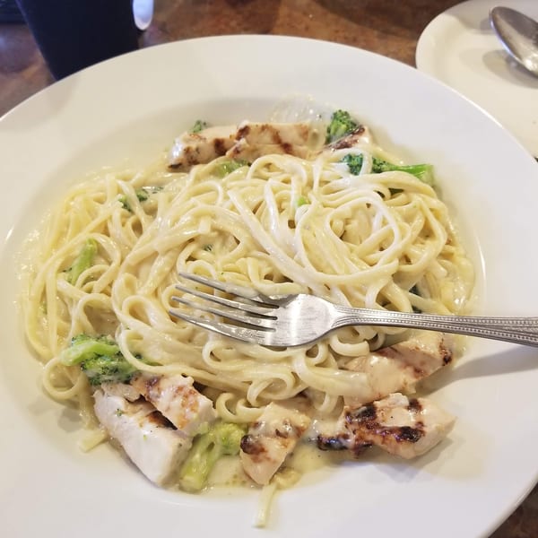 Fettuccine Alfredo with grilled chicken and broccoli, with a fork resting on the pasta.