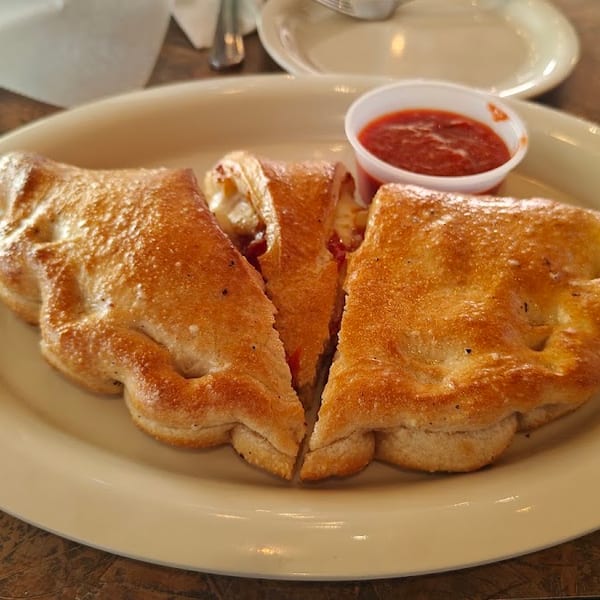 Golden-brown calzone, sliced into three pieces, with a side of marinara sauce on a white plate.