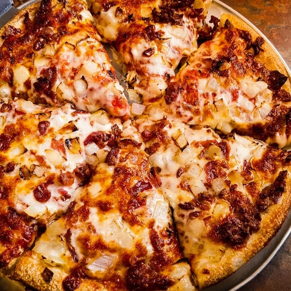A freshly baked pizza with caramelized onions and bacon, with one slice removed, next to a fork and knife.