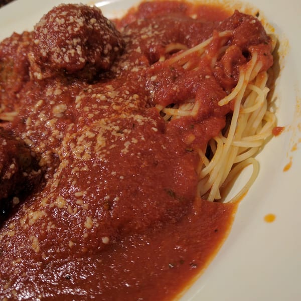 Spaghetti and meatballs covered in red sauce and grated cheese on a white plate.