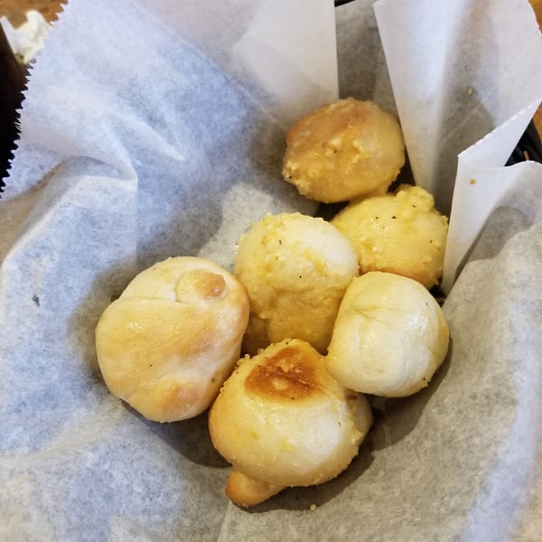 A basket of golden-brown garlic knots, some with visible seasoning, nestled in white parchment paper.